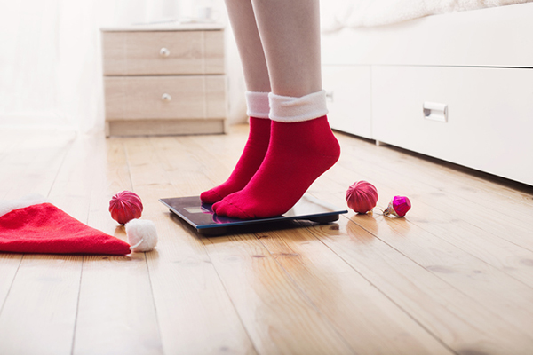 Female feet standing on electronic scales for weight control in red socks with Christmas decoration