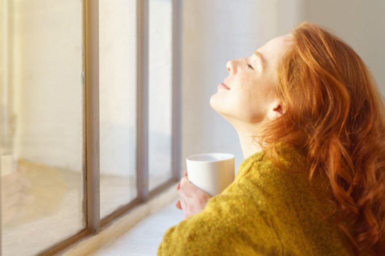 schöne frau genießt die sonnenstrahlen am fenster